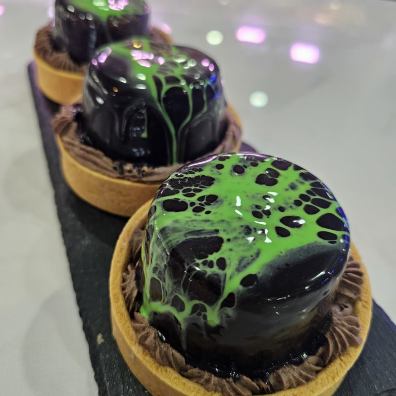 Trois petits gâteaux individuels sur un plateau noir. Chaque gâteau est recouvert d'un glaçage vert foncé marbré.