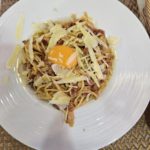 Un plat de pâtes carbonara avec un jaune d'œuf cru au centre, parsemé de fromage râpé et de morceaux de chorizo.