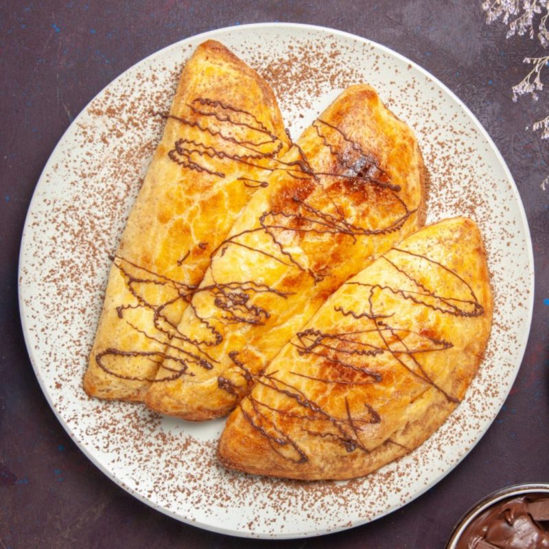 Trois chaussons aux pommes dorés disposés sur une assiette blanche. Les chaussons sont garnis de pommes et recouverts de sucre glace.