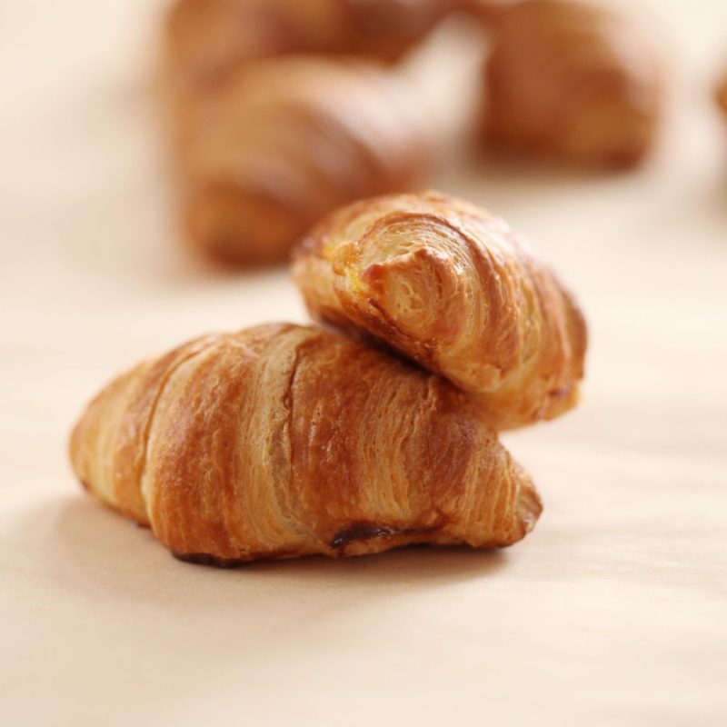 Deux mini croissants aux amandes dorés, posés l'un sur l'autre, sur un fond blanc.