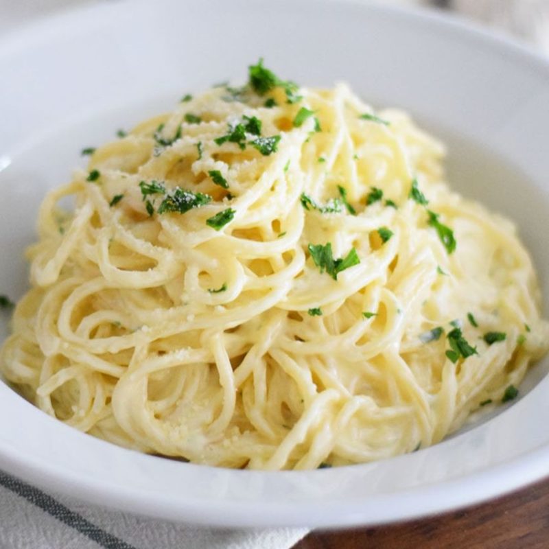 Un plat de spaghetti enroulés dans une sauce crémeuse et onctueuse, parsemé de fromage râpé et de quelques feuilles de persil frais.